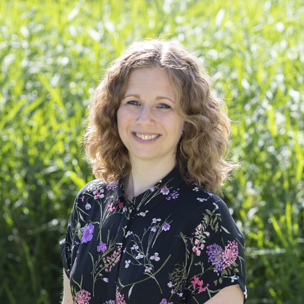 Natalie Hensen, eigenaar Webgrrl. Vriendelijk lachende jonge vrouw, met middelblond halflang krullend haar, zwart gebloemde blouse, tegen achtergrond met gras.